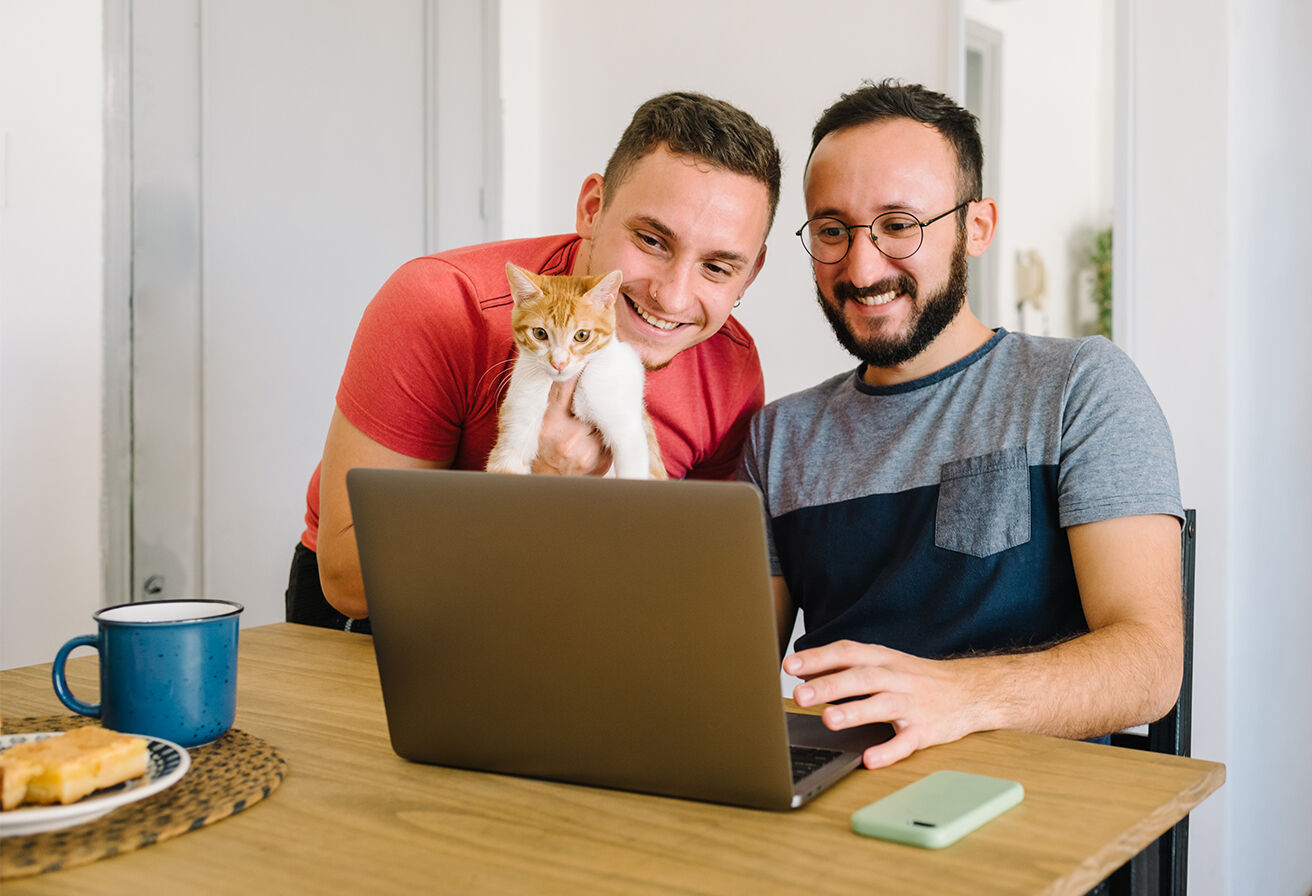 couple holding cat and looking at laptop